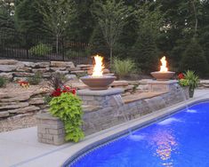 two fire bowls sitting on top of a stone wall next to a swimming pool