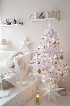 a white christmas tree with gold and silver ornaments on it, next to a bed