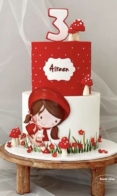 a red and white cake with a girl on it's side, surrounded by mushrooms