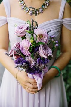 a woman in a dress holding a bouquet of flowers and wearing a necklace on her neck