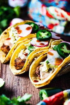 several tacos are lined up on a wooden table with green peppers and other toppings