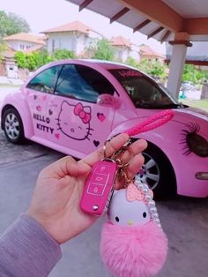 a person holding a pink hello kitty keychain in front of a pink car