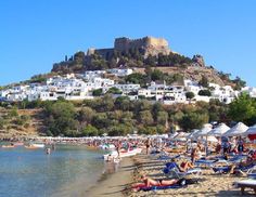 many people are relaxing on the beach in front of an old castle and white buildings