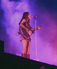 a woman standing on top of a stage holding a guitar