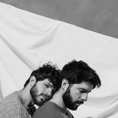 two men looking at their cell phones while standing next to each other in front of a white backdrop