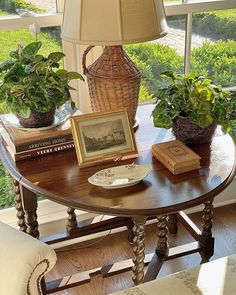 a table with some books and plants on it in front of a window that looks out onto the yard