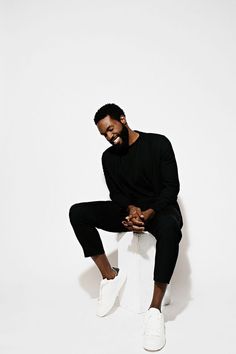 a man sitting on top of a white box wearing black pants and a black sweater