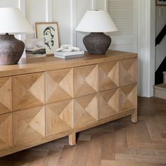 two lamps on top of a dresser in a room with wood floors and white walls