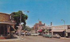 an old photo of cars parked on the side of the road in front of shops