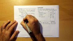 a person writing on a piece of paper with a pen in their left hand and another hand holding a ballpoint pen next to it