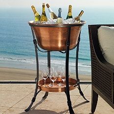 a table with wine glasses and bottles on it next to the ocean in front of a chair