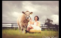 a woman sitting on a chair next to a cow in a field with cloudy skies