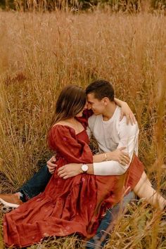 a man and woman are sitting in the tall grass with their arms around each other