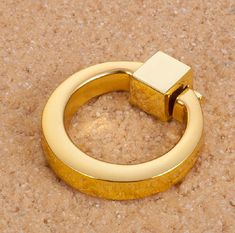 a gold colored ring with a small square object on the top and bottom, sitting on a tan surface