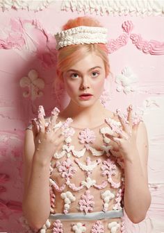 a woman with pink hair wearing a tiara and holding her hands in front of her face