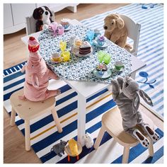 two stuffed animals sitting at a table with tea cups and other toys on the floor