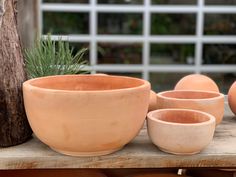 several clay pots and bowls sitting on a wooden table next to a potted plant