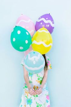 a girl holding balloons in her hands and wearing a dress with flowers on it, against a blue background