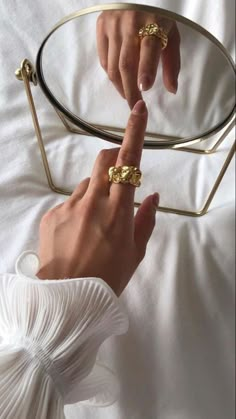 two hands touching each other on a bed with white sheets and gold rings in the middle