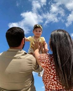 a man holding a baby up in the air while standing next to a woman and child