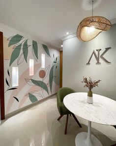 a white table sitting in front of a wall with leaves painted on it and two green chairs