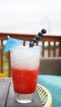 a red, white and blue drink sitting on top of a table next to an umbrella