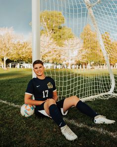 a young man sitting on the ground next to a soccer ball in front of a goal