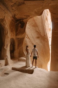 a man and woman holding hands standing in an area with large rocks on either side