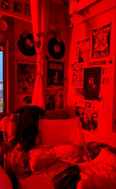 a bedroom with red light coming from the window and posters on the wall above it