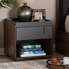 a nightstand with some books and a vase on it next to a table with a lamp