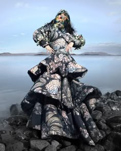 a woman is standing on rocks by the water wearing a long black and white dress