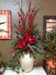 a white vase filled with red flowers and greenery on top of a table next to a mirror