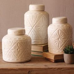 three white ceramic jars sitting on top of a wooden table next to a potted plant