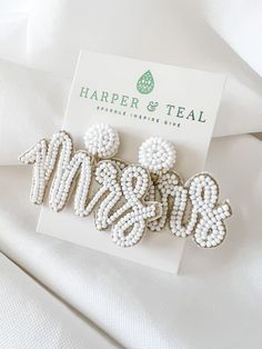 three white beaded earrings sitting on top of a piece of paper next to a business card