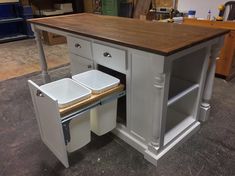 a kitchen island with two trash cans in the middle and an open cabinet on top