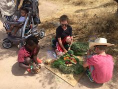 three children are sitting on the ground with vegetables