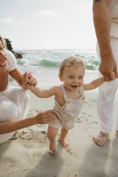 a woman holding the hand of a little boy while standing on top of a sandy beach