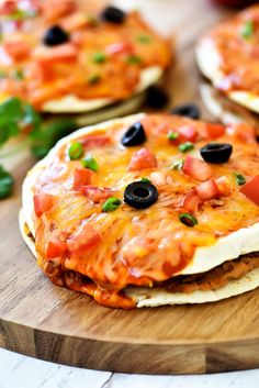 mexican pizza with black olives and tomatoes on a wooden cutting board next to other food items