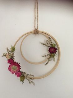 two circular wooden hoop with flowers hanging from it's sides on a string attached to the wall