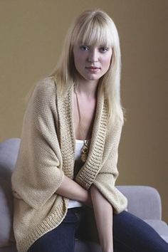 a blonde woman sitting on top of a couch wearing a cardigan sweater and jeans