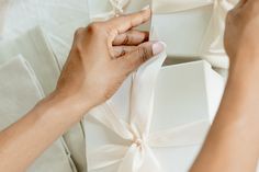 a woman is wrapping a white gift box with a bow on it's side