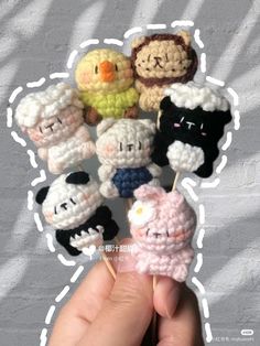 a hand holding several small crocheted animals on toothpicks in front of a white wall