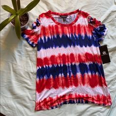 a red, white and blue shirt sitting on top of a bed next to a plant