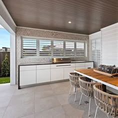 an outdoor kitchen with wooden table and wicker chairs, white cabinets and counter tops