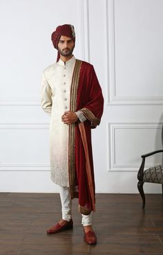 a man in a white and red outfit standing on a hard wood floor with a chair behind him