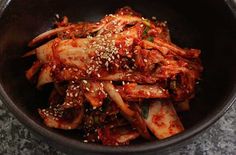 a black bowl filled with meat and vegetables covered in sesame seed sprinkles