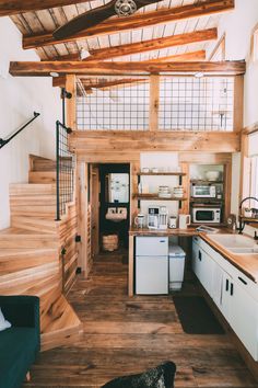 a kitchen with wooden floors and white appliances in a small cabin style home that has stairs leading up to the second floor