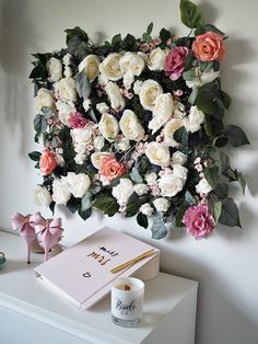 a white and pink flower arrangement on a wall above a desk with a candle, notepad, and book