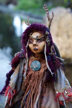 a stuffed animal with horns and feathers on it's head standing in front of water