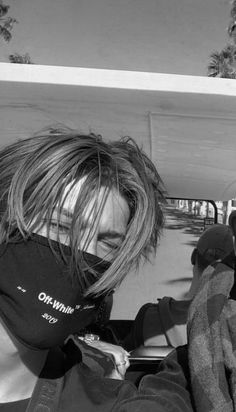 a woman wearing a neck gaiter in the back of a car with palm trees behind her